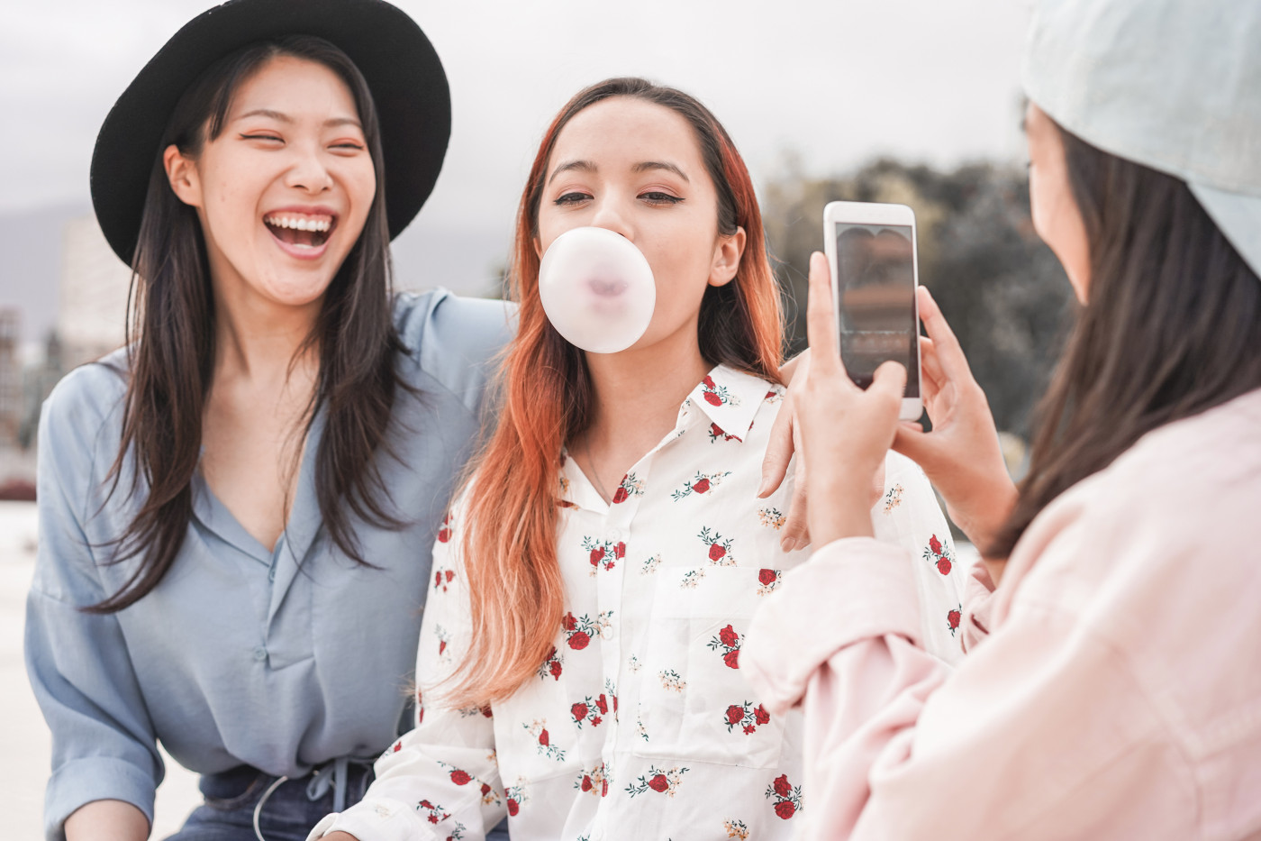 Three young friends in colorful glasses cheerfully blowing bubbles with gum. 