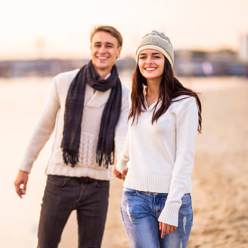 Young couple walking down the beach smiling holding hands 