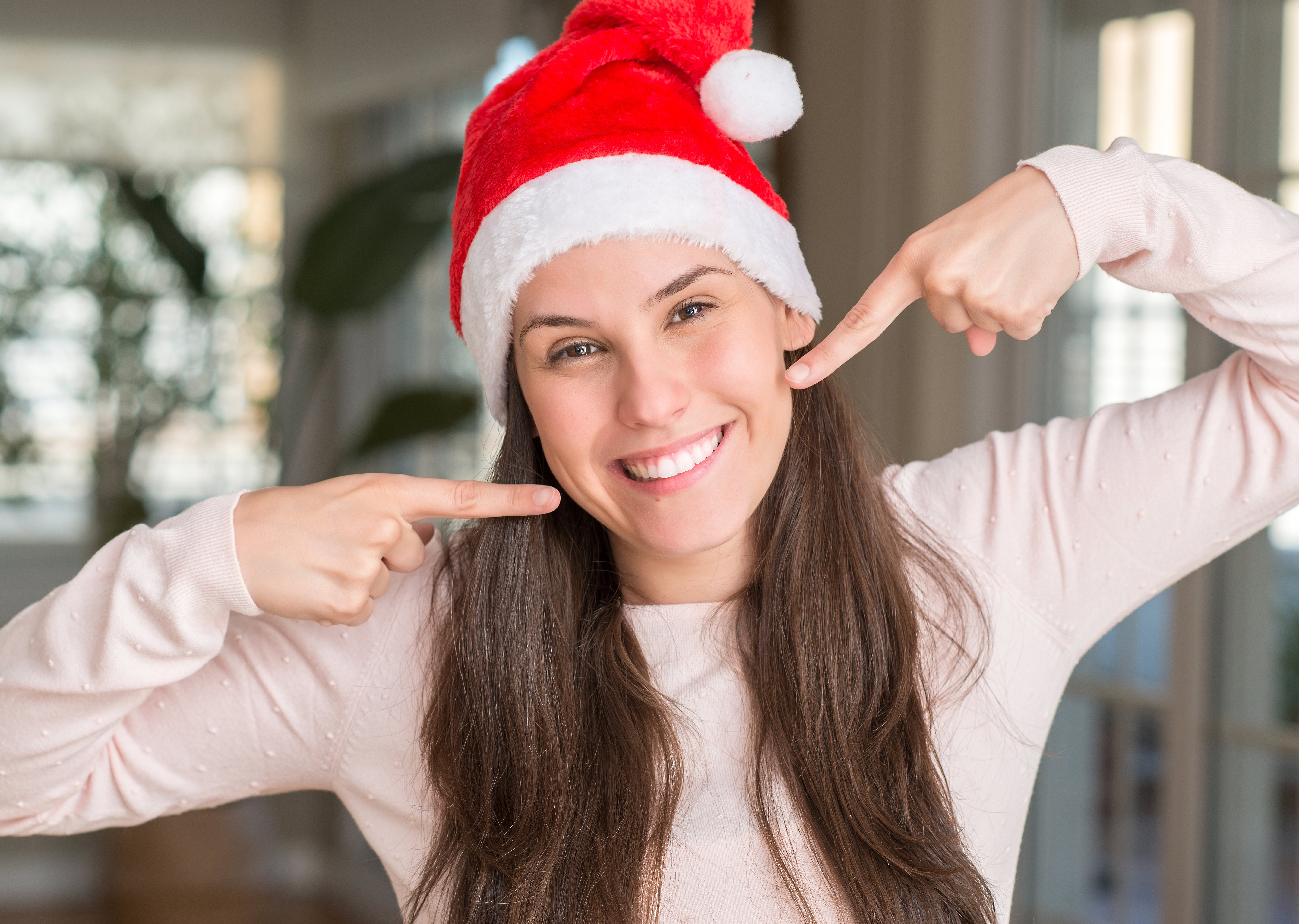 Young couple wearing Santa hats smiling while cheerfully pointing to their teeth.