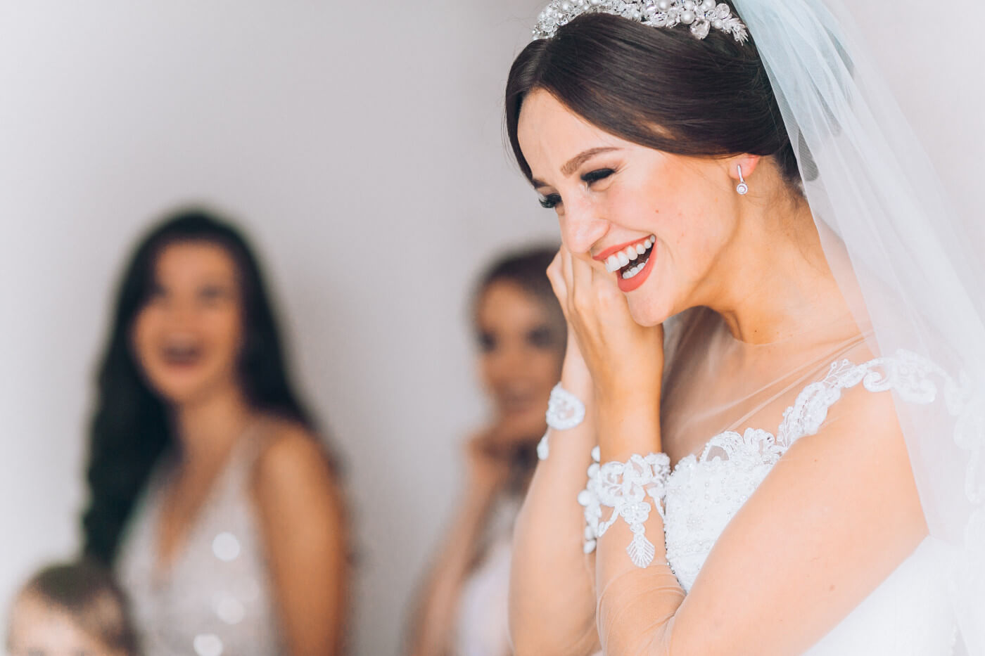  Bride laughing in a room with bridesmaids while putting on an earring.  