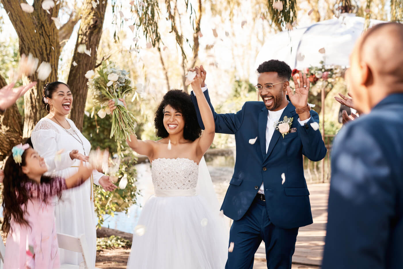 Bride and groom walk down the aisle hand in hand, smiling joyfully, while their friends cheer in the background.