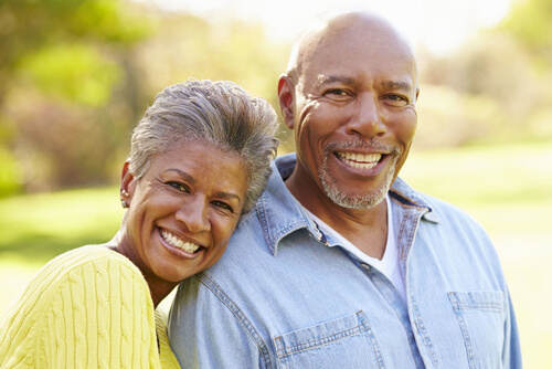 Elderly man and woman with healthy smiles hugging in park during fall season